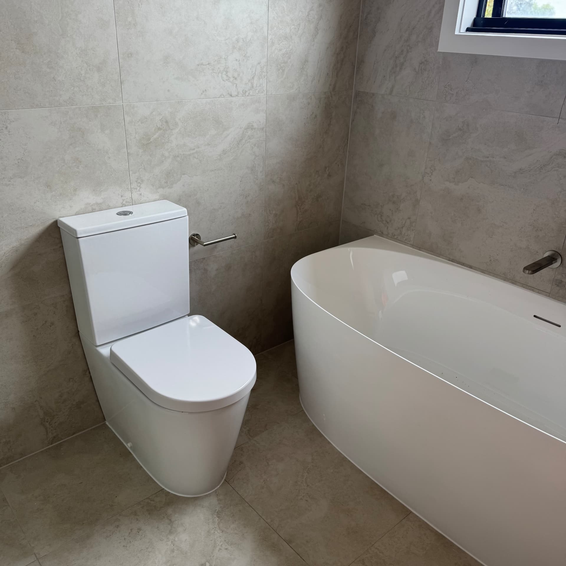 Toilet and bath sealed against travertine-look tiled walls and floor