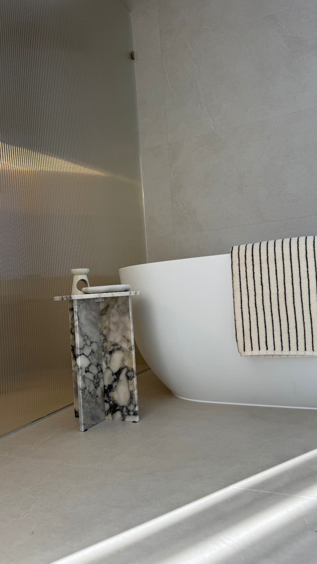 Freestanding bath sealed against fluted glass and tiled walls