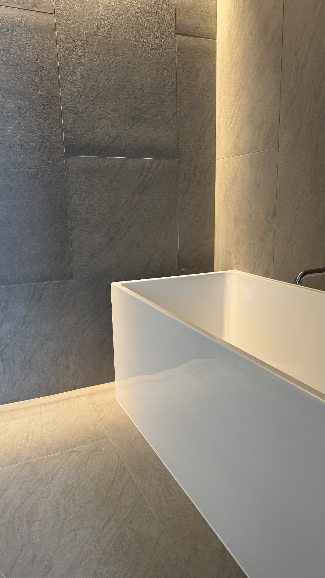 Rectangular bath sealed against stone-look tiled walls