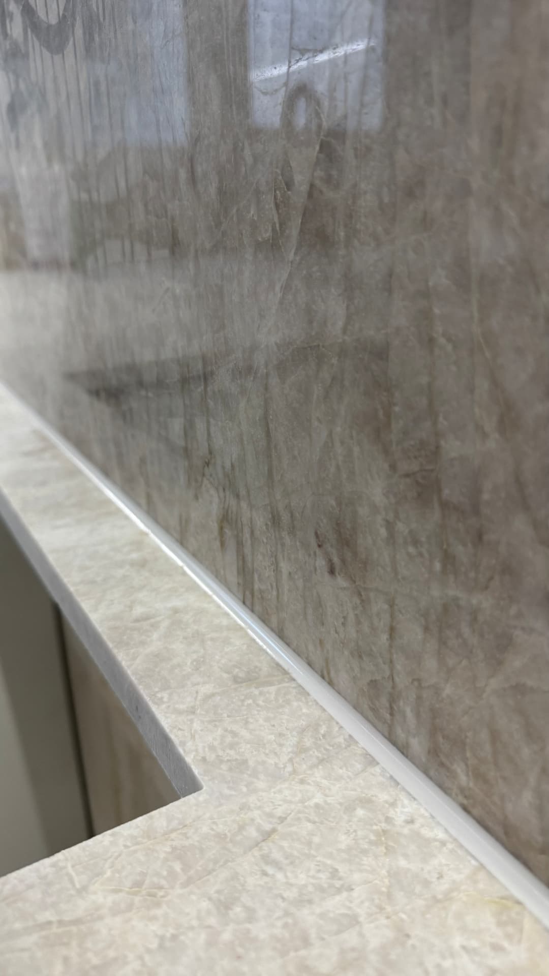 Close-up of a fine white silicone bead along a stone splashback