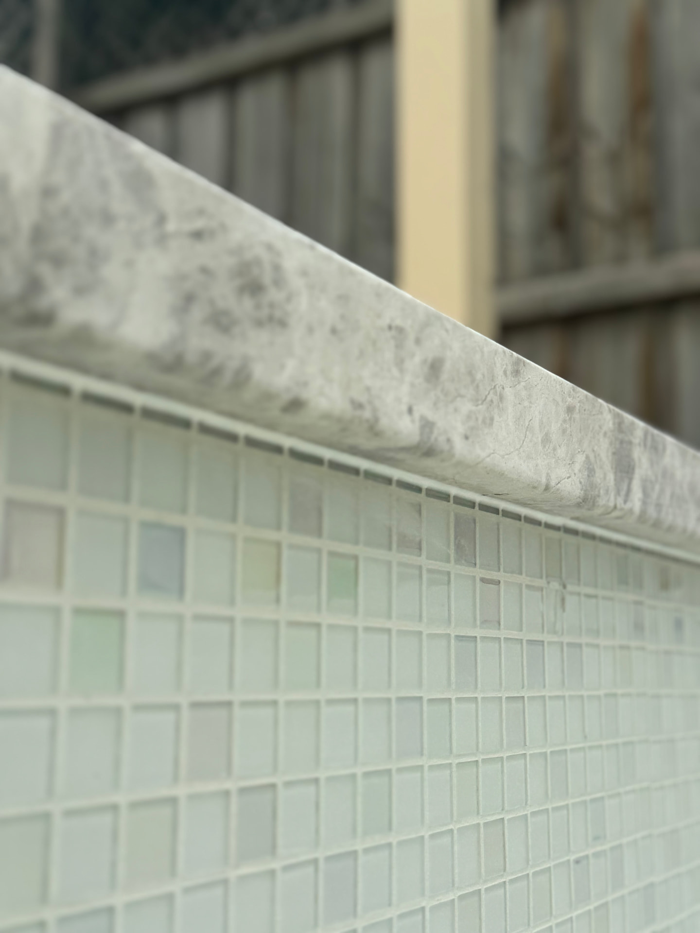 Pool coping sealed to glass mosaic tiled wall